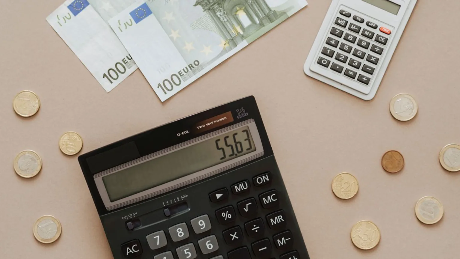 Calculatrice, billets en euros et pièces posés sur un plan de travail